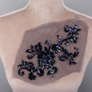 May include: Black floral applique with sequins on a sheer mesh fabric. The applique features a large flower with smaller flowers and leaves.