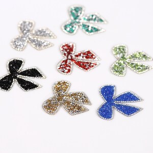 seven glittery, colorful bow-shaped objects arranged on a white background.