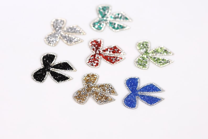 seven glittery, colorful bow-shaped objects arranged on a white background.
