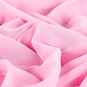 The image is a close-up of a soft, flowing pink fabric, possibly silk or chiffon, with a slightly wrinkled texture.