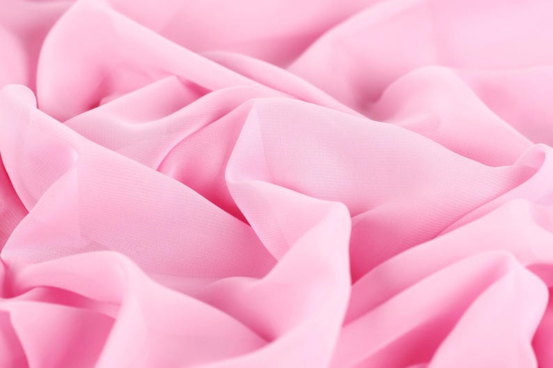 The image is a close-up of a soft, flowing pink fabric, possibly silk or chiffon, with a slightly wrinkled texture.
