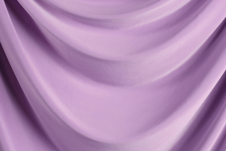 The image is a close-up of a soft, flowing purple fabric, possibly a curtain or garment. The fabric has a smooth, shiny texture and is draped in a way that creates a sense of movement and depth.