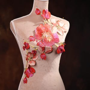 Puede incluir: Una delicada aplicación floral con flores rojas y rosas, ideal para añadir un toque de elegancia a la ropa o las manualidades.