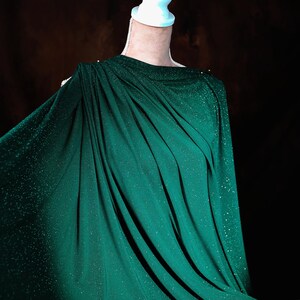 A mannequin wearing a green, sparkly fabric draped over its body.