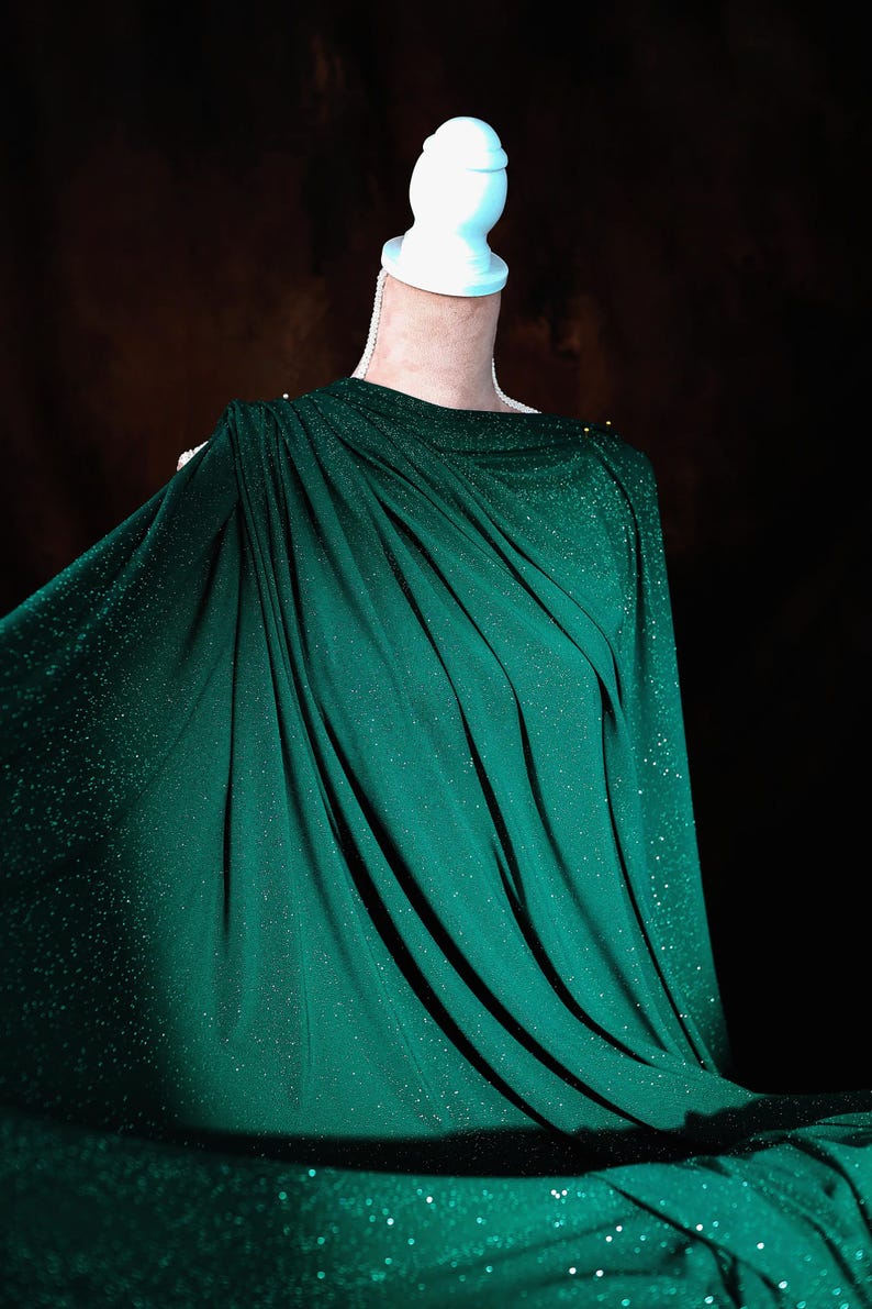 A mannequin wearing a green, sparkly fabric draped over its body.