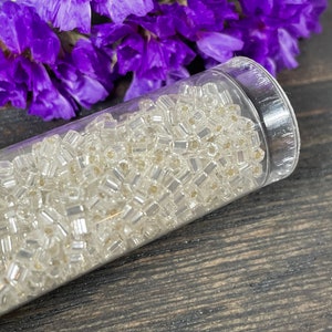 May include: A clear plastic tube filled with small, clear glass beads. The beads have a slightly iridescent finish.