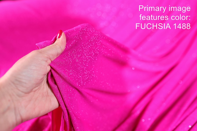 A hand is holding a piece of fabric with a bright pink color and sparkly texture, against a background of a similar pink fabric.