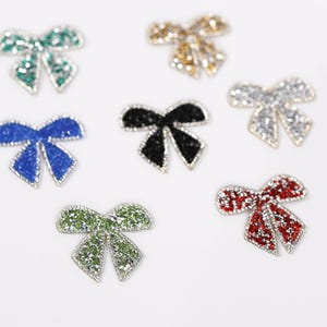 six small, colorful, and sparkling bow-shaped objects arranged on a white background.