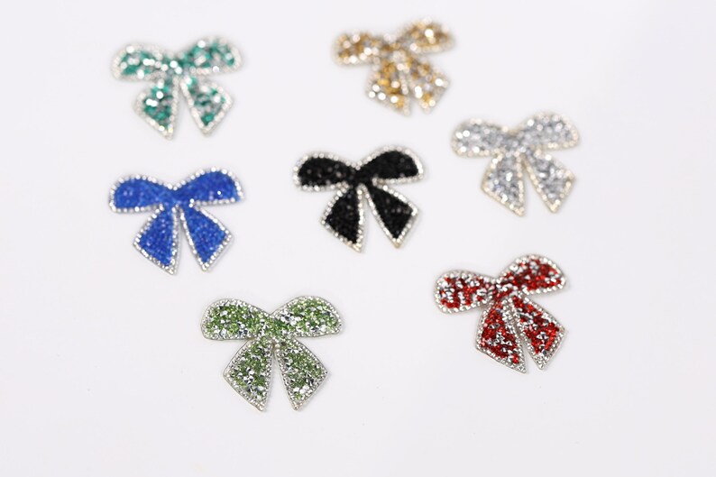 six small, colorful, and sparkling bow-shaped objects arranged on a white background.