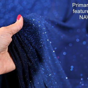 A hand holding a piece of navy blue fabric with a glittery texture, against a background of a blue fabric with white dots.