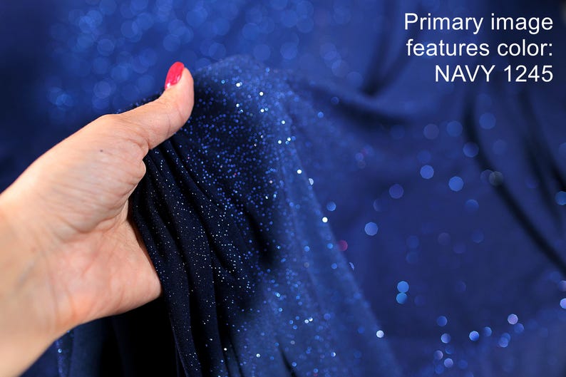 A hand holding a piece of navy blue fabric with a glittery texture, against a background of a blue fabric with white dots.