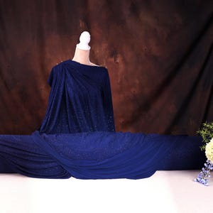a mannequin wearing a blue dress with a draped, flowing design, placed on a white table. Next to the mannequin is a vase filled with flowers, creating a visually appealing and elegant display.