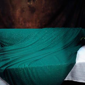 a green fabric with sparkles, a white tablecloth, and a vase with pink flowers.