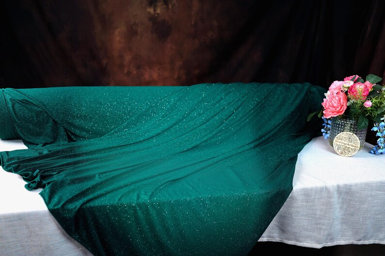 a green fabric with sparkles, a white tablecloth, and a vase with pink flowers.