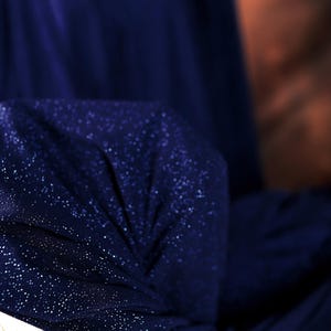 a close-up view of a dark blue fabric with a sparkling texture, possibly a piece of clothing or a decorative item.