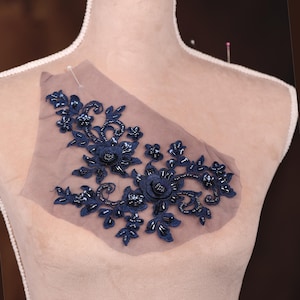 May include: Navy blue beaded floral applique with a sheer mesh backing. The applique features a cluster of three dimensional flowers with beaded accents.