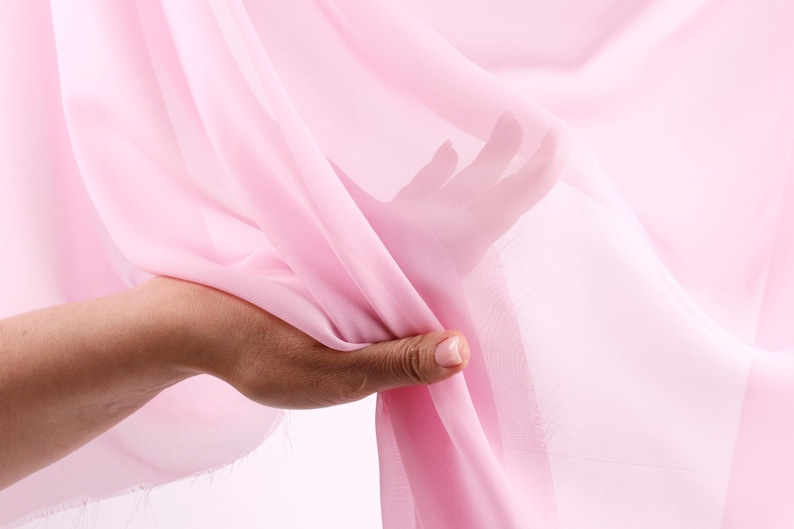 A hand is holding a pink fabric, with the fabric partially covering the hand and fingers.
