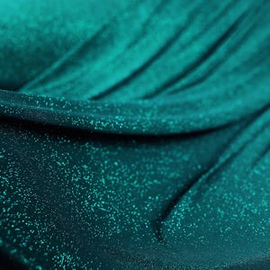 a close-up view of a shiny, turquoise-colored fabric with a glittery texture, creating a sparkling effect.