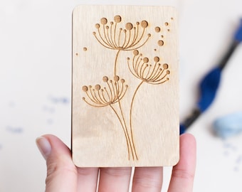 May include: A wooden card with a laser-cut design of three stylized dandelions with round seed heads.