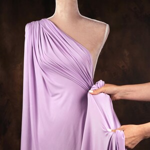 A mannequin wearing a lavender one-shoulder dress is being adjusted by someone's hands.