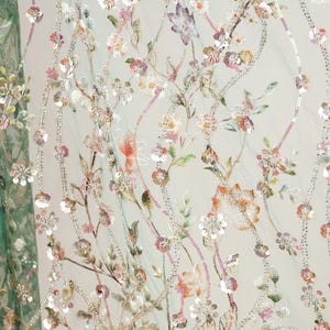 a close-up view of a fabric with a floral pattern, including various shades of pink, green, and white flowers and leaves. The fabric appears to be made of a sheer material, giving it a delicate and airy appearance. The intricate details and vibrant colors of the floral design create a visually appealing and eye-catching pattern.