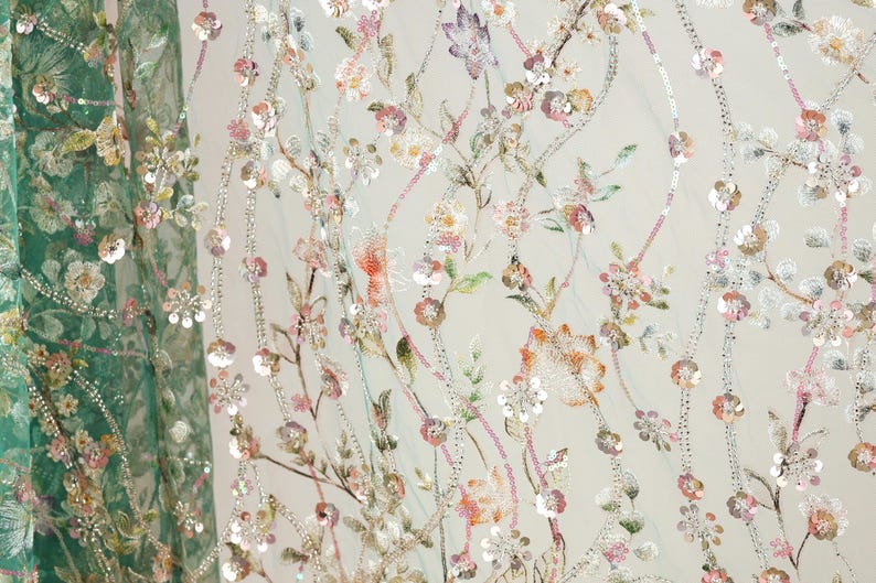 a close-up view of a fabric with a floral pattern, including various shades of pink, green, and white flowers and leaves. The fabric appears to be made of a sheer material, giving it a delicate and airy appearance. The intricate details and vibrant colors of the floral design create a visually appealing and eye-catching pattern.