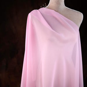 A mannequin wearing a pink, sheer fabric draped over its shoulder.