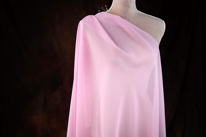 A mannequin wearing a pink, sheer fabric draped over its shoulder.