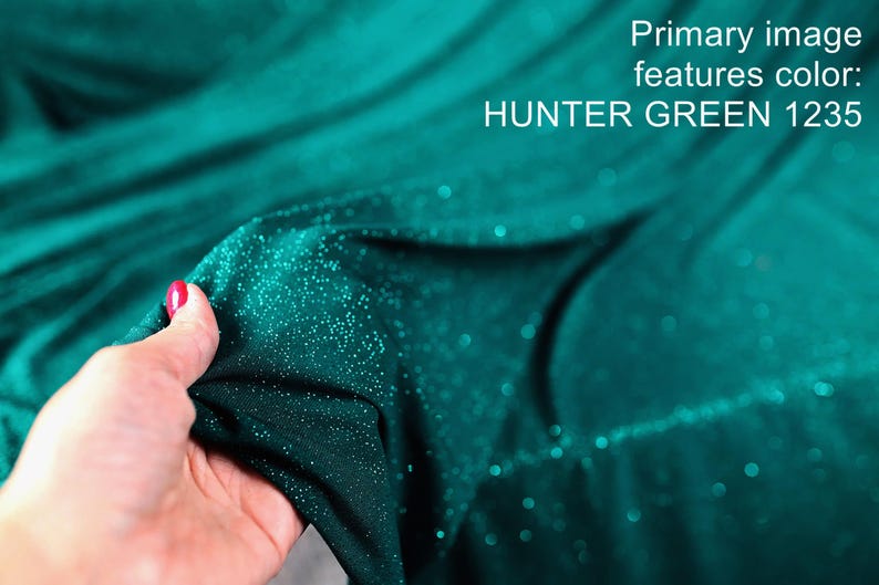 A hand holding a piece of fabric with a shimmering green color, likely Hunter Green, against a blurred teal background.