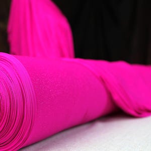 A close-up image of a bright pink fabric roll, possibly a piece of clothing or textile, resting on a surface.