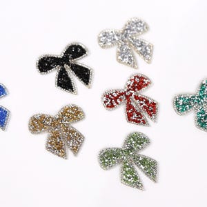 seven glittery bow-shaped objects in various colors, including blue, black, red, green, gold, and silver.