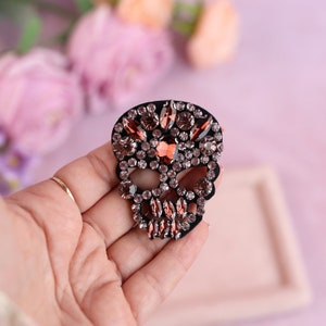 May include: A black skull-shaped patch decorated with brown and clear rhinestones.