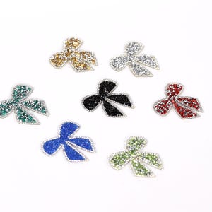 seven small, colorful, glittery bows arranged in a circular pattern on a white background.