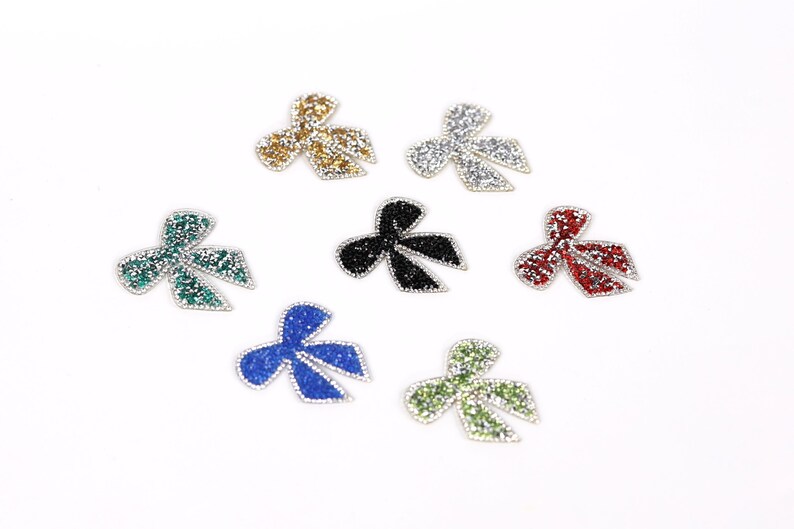seven small, colorful, glittery bows arranged in a circular pattern on a white background.