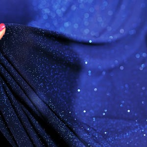 A hand holding a piece of blue fabric with sparkles on it.
