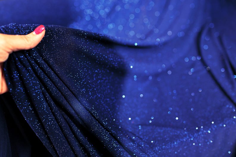 A hand holding a piece of blue fabric with sparkles on it.