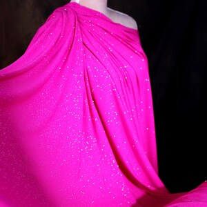 A close-up of a bright pink fabric with sparkles, draped over a person's body.