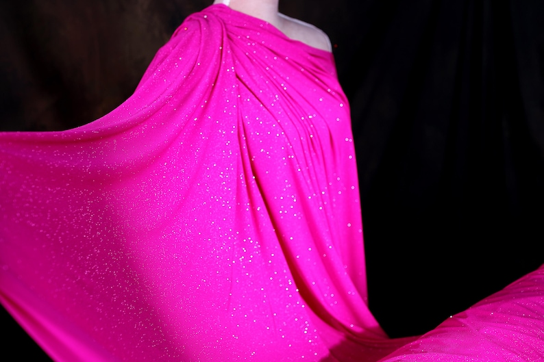 A close-up of a bright pink fabric with sparkles, draped over a person's body.