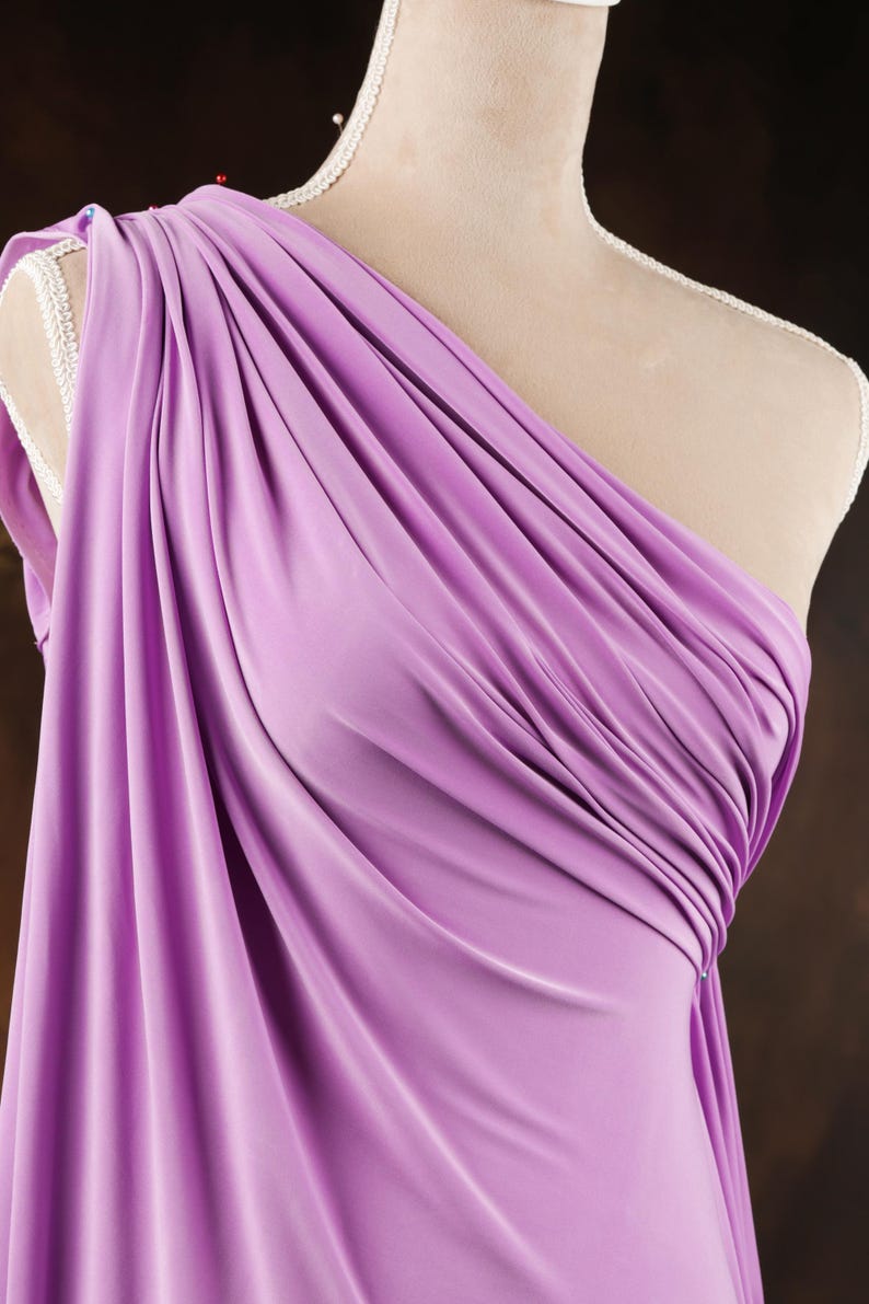 A mannequin wearing a purple one-shoulder dress with a draped, flowing fabric.
