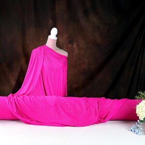 a mannequin wearing a bright pink one-shoulder dress, placed on a white tablecloth. Next to the mannequin is a vase filled with flowers, creating a visually appealing display.