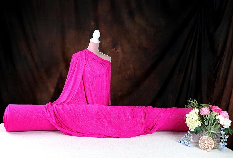 a mannequin wearing a bright pink one-shoulder dress, placed on a white tablecloth. Next to the mannequin is a vase filled with flowers, creating a visually appealing display.