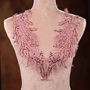May include: A pink beaded and sequined lace applique with a V-neck shape. The applique is perfect for adding a touch of elegance to any garment.