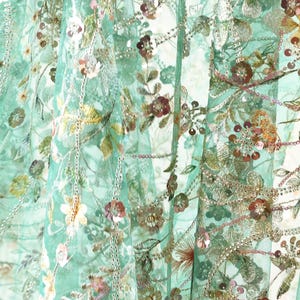 The image is a close-up of a fabric with a floral pattern, featuring various shades of green, pink, and yellow flowers and leaves. The fabric appears to be made of a sheer material, giving it a delicate and airy appearance.