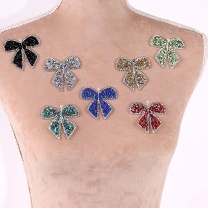 a mannequin with a beige fabric torso, adorned with a collection of seven colorful, sparkling rhinestone-encrusted bows in various shapes and sizes.