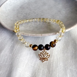 May include: A gold bracelet with clear and yellow beads and a tiger's eye charm. A gold lotus charm hangs from the bracelet.