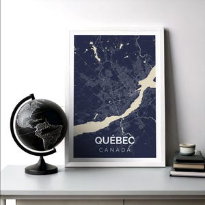 May include: A framed print of a map of Quebec City, Canada. The map is in a dark blue colour with white lines showing the streets and a beige river. The text "QUEBEC CANADA" is printed at the bottom of the map.