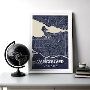 May include: A framed print of a map of Vancouver, Canada. The map is in a dark blue color with white lines showing the streets and waterways. The city name and country are printed in white at the bottom of the map.