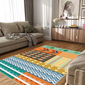 May include: A rectangular area rug featuring a vibrant geometric pattern with sections of orange, teal, mustard yellow, and brown. The design includes repeating chevrons, diamonds, stripes, and small triangles arranged in a colorful patchwork layout.