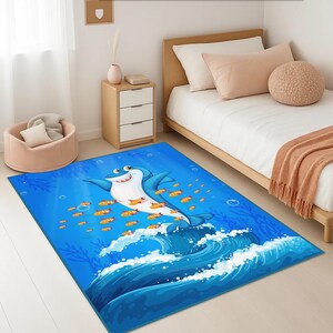 May include: A rectangular blue rug with a cartoon shark design. The shark is light blue with a white belly and orange fish. The rug depicts a marine scene with waves, bubbles, and seaweed, suitable for a child's room.