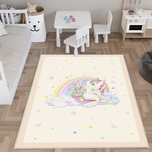 Può includere: Un tappeto bianco e crema con un design di unicorno e arcobaleno. L'unicorno è seduto su una nuvola con un castello dietro. Il tappeto ha un bordo rosa chiaro.